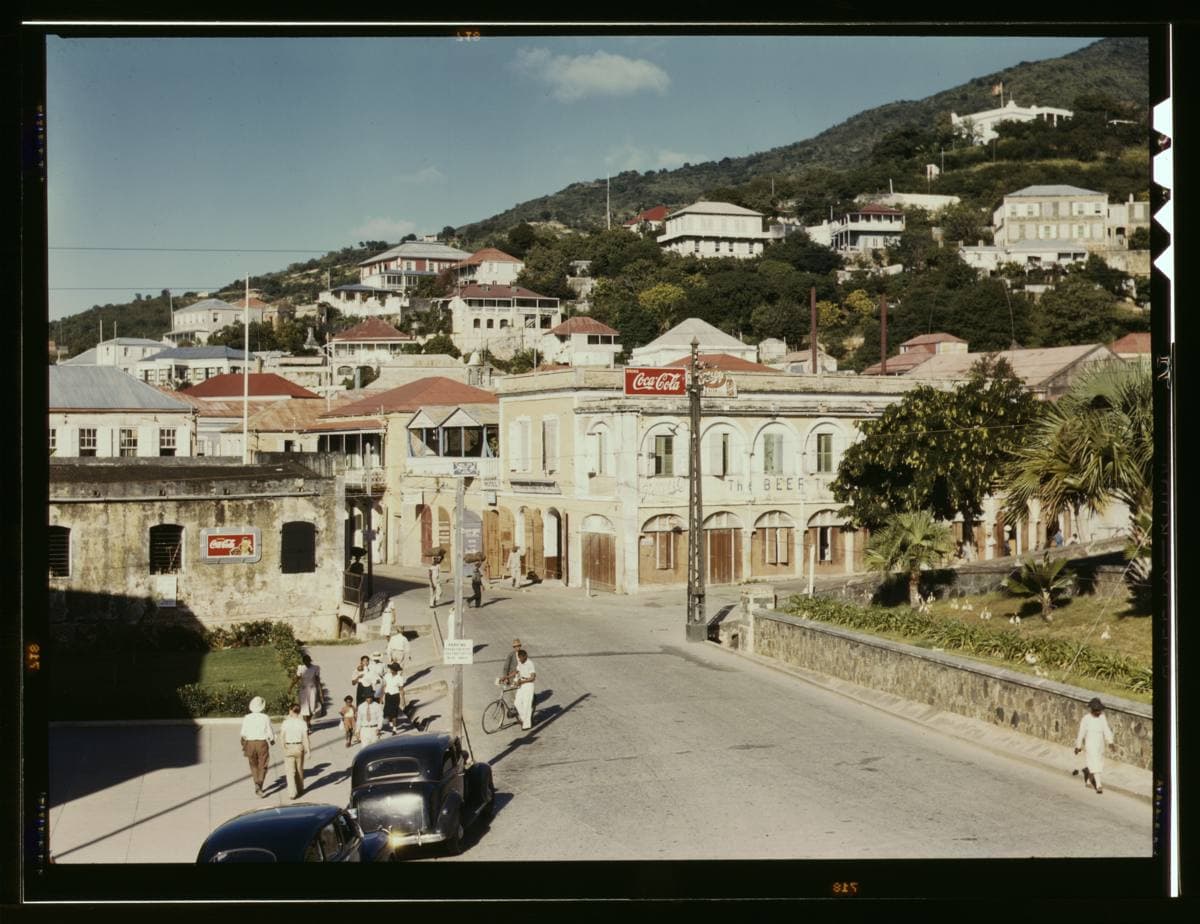 A colour view down a sunny Caribbean main street lined with old stone shopfronts