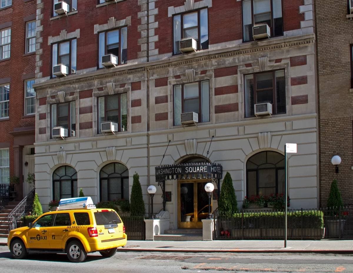 A brick and stone hotel front with an awning and a yellow taxi outside