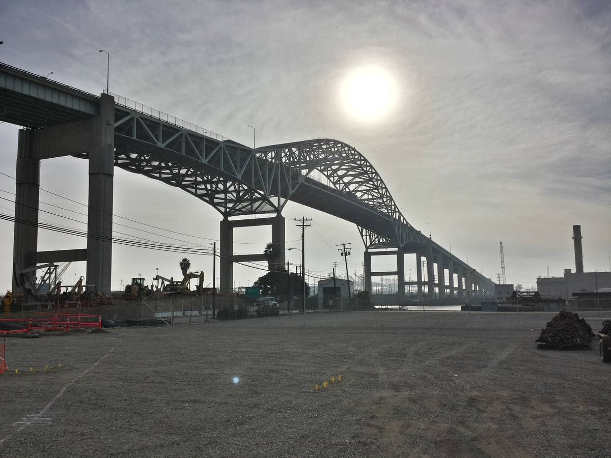A steel arch bridge over a harbour channel with cranes beyond