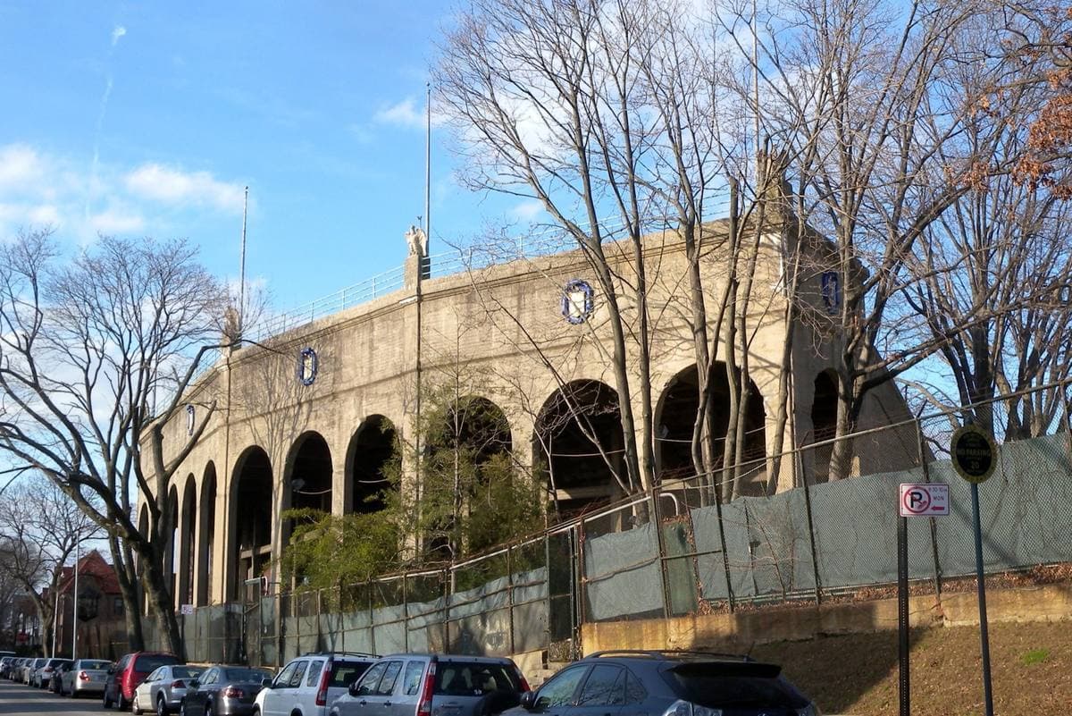 The arched concrete outer wall of a 1920s stadium behind bare trees