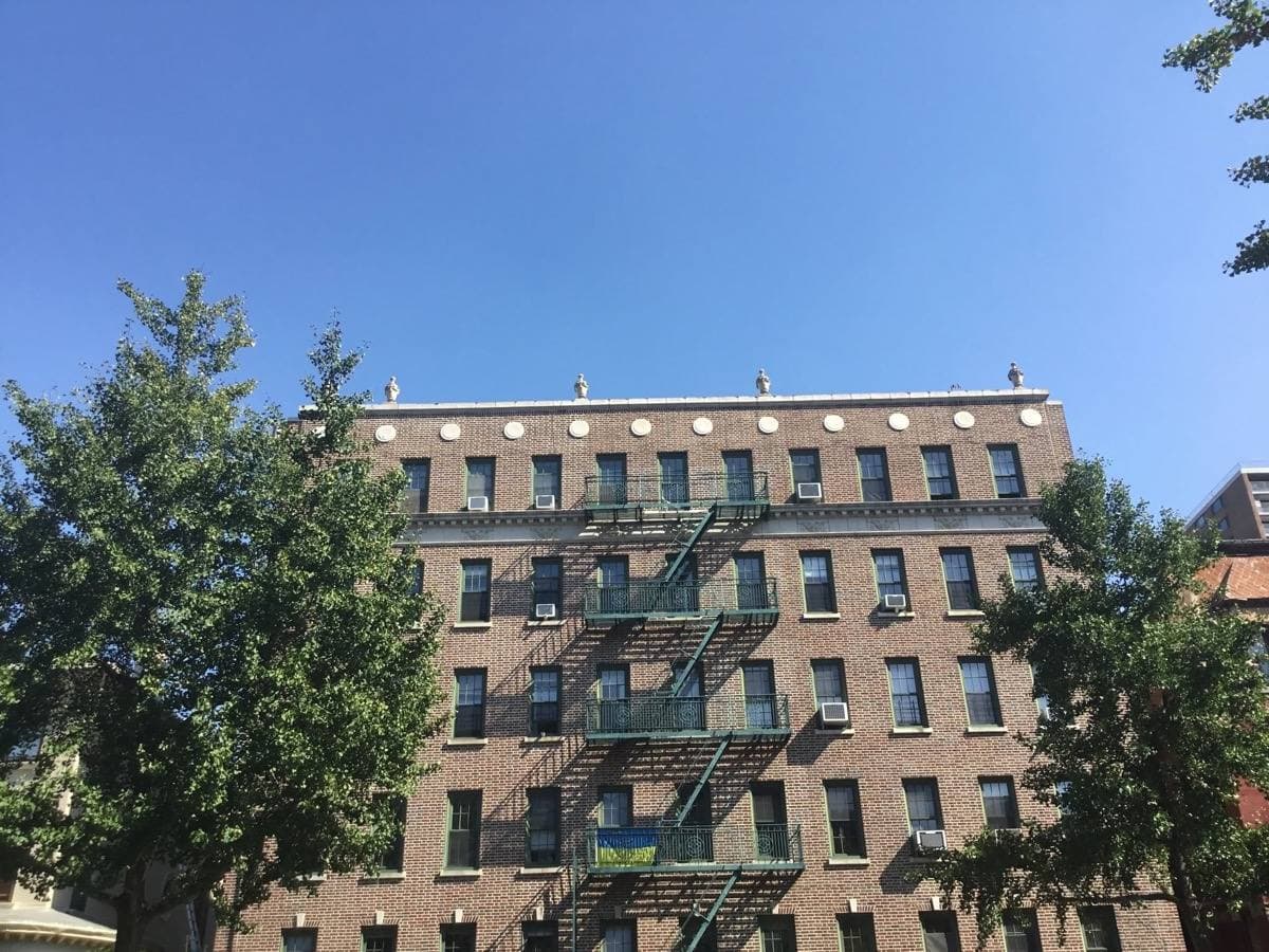A brick apartment block with zig-zag fire escapes against a blue sky, Clinton Hill