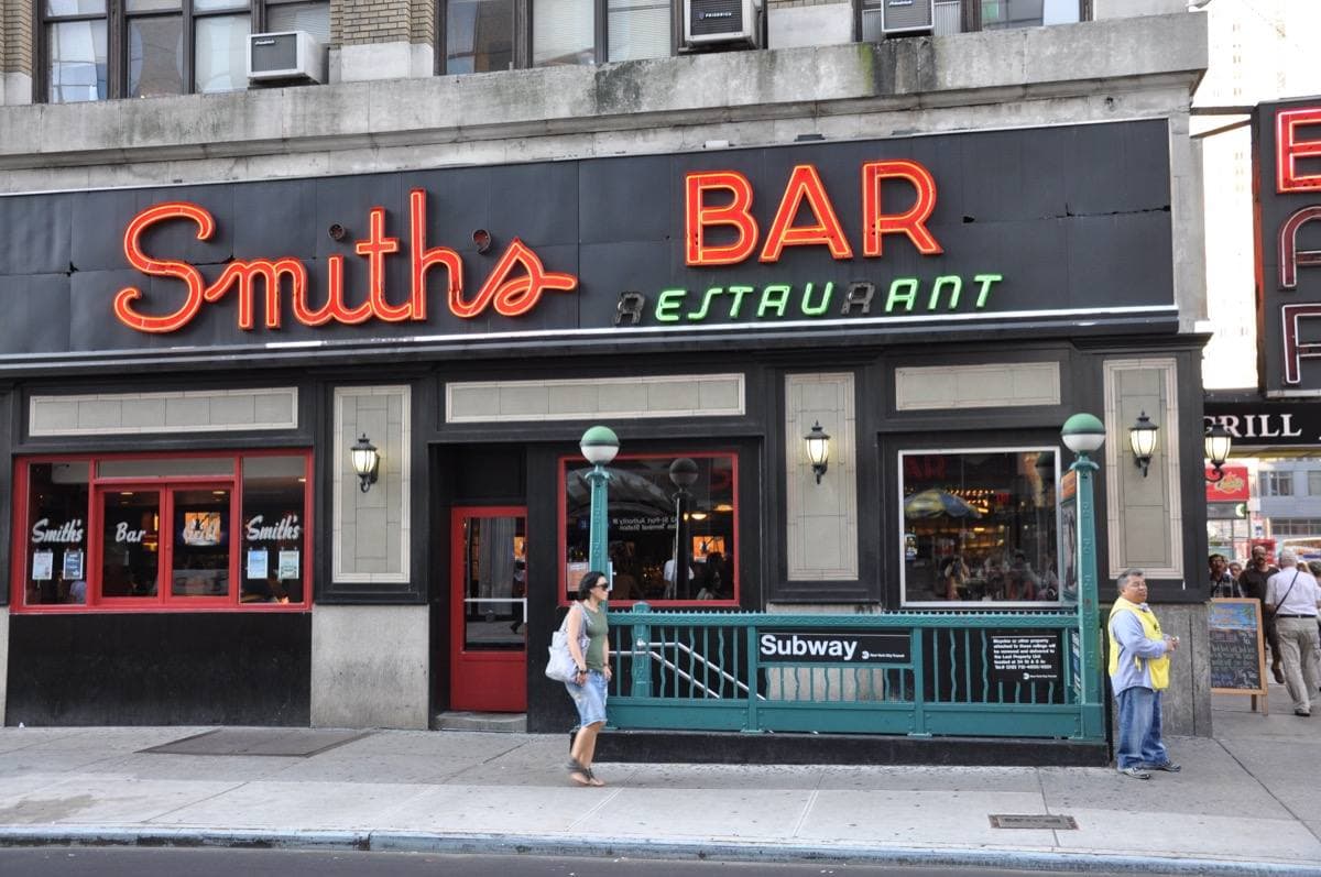 A diner-bar front with red neon letters and a subway entrance on Eighth Avenue