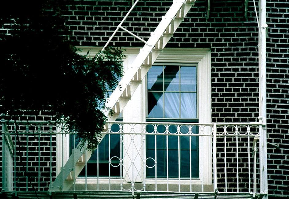 A black iron fire escape across a brick wall and a tall window, Fulton Street, 1997