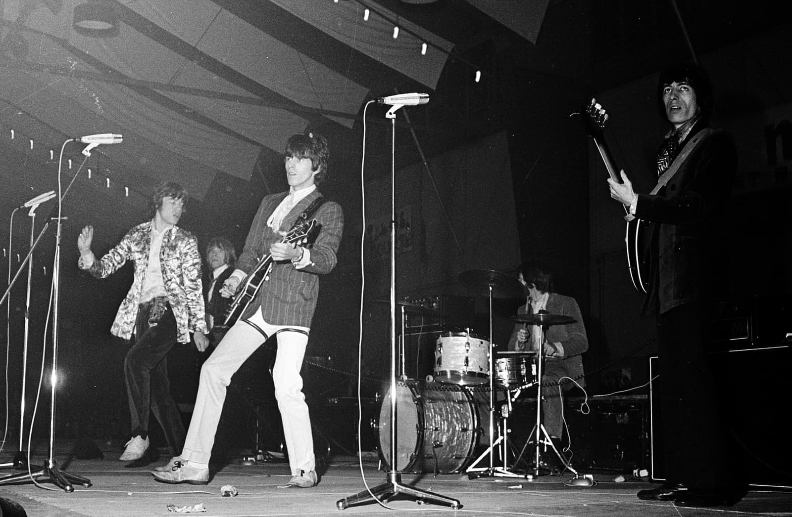 The band on a bare stage, guitars up, drum kit behind