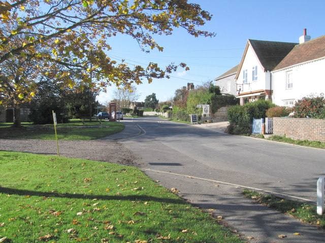A village lane and green in West Wittering under a blue sky