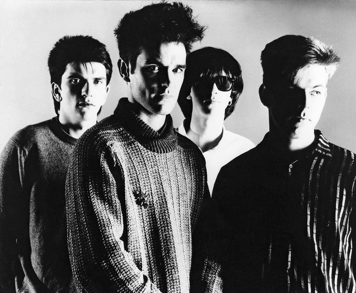 Black-and-white portrait of the four Smiths, Morrissey in a chunky knitted jumper at the front, Johnny Marr in dark glasses behind