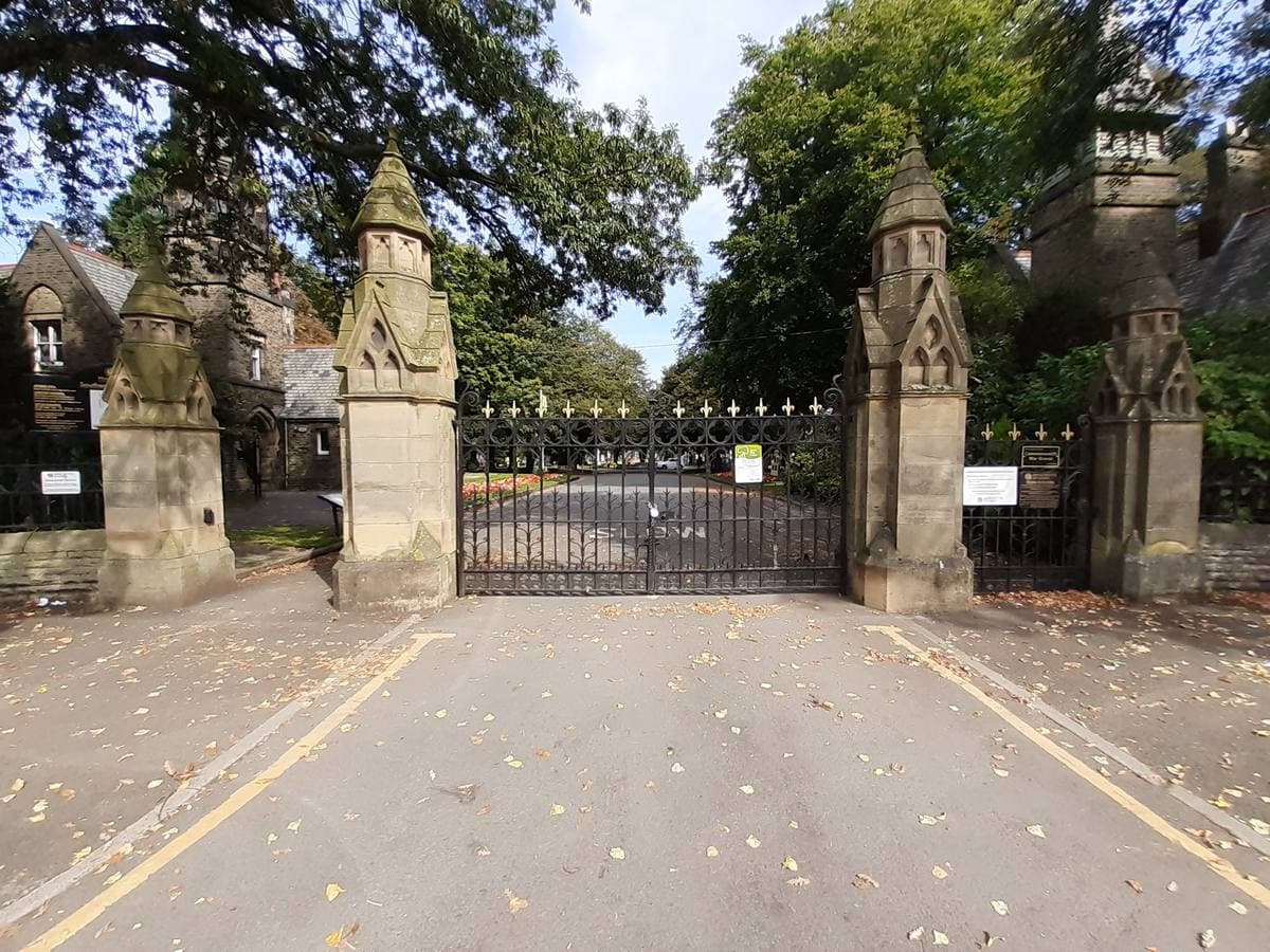 Stone gate piers and closed iron gates under trees, a road leading in