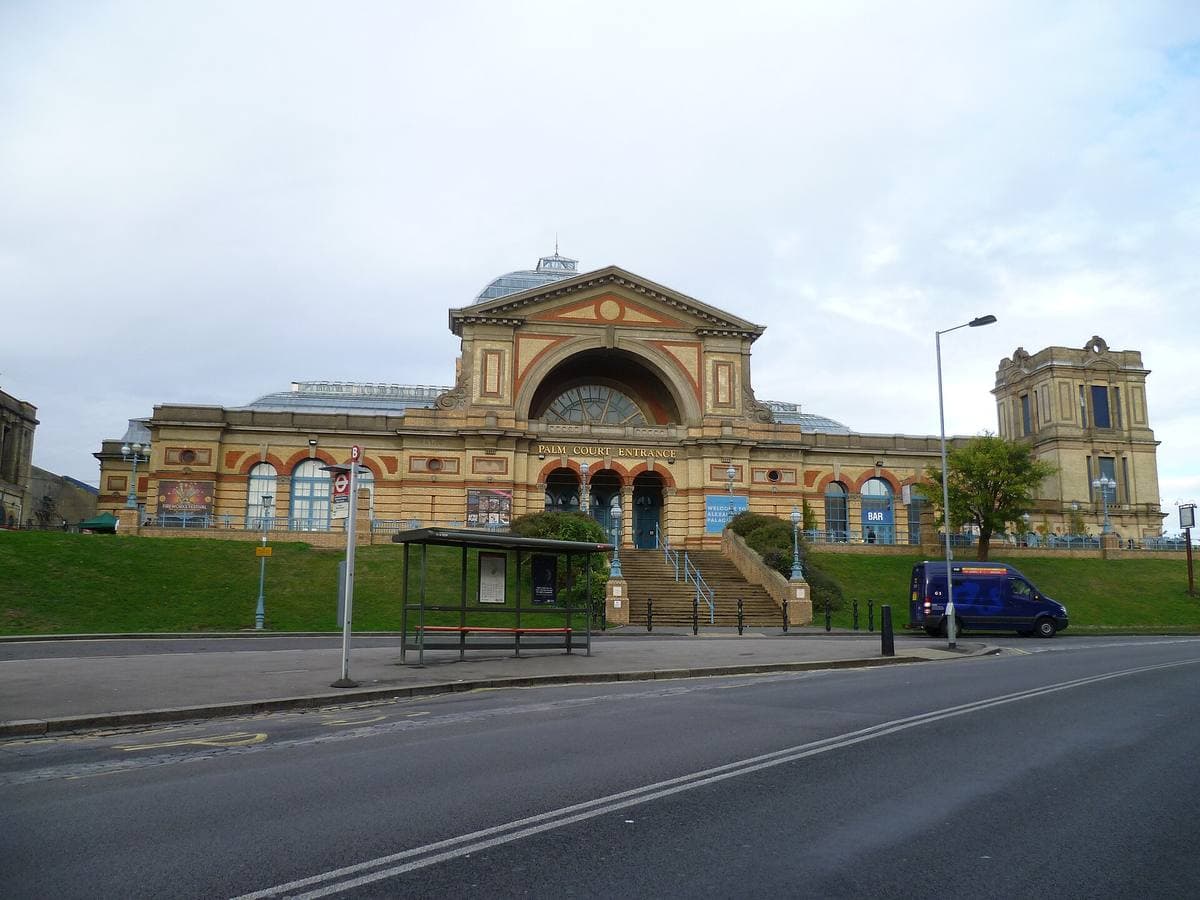 A long Victorian palace of yellow brick with a great arched rose window above a grassy bank