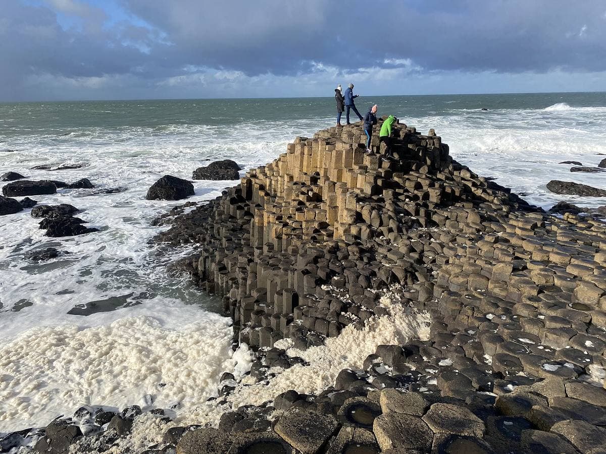 Dark hexagonal basalt columns stepping into a churning sea of white foam