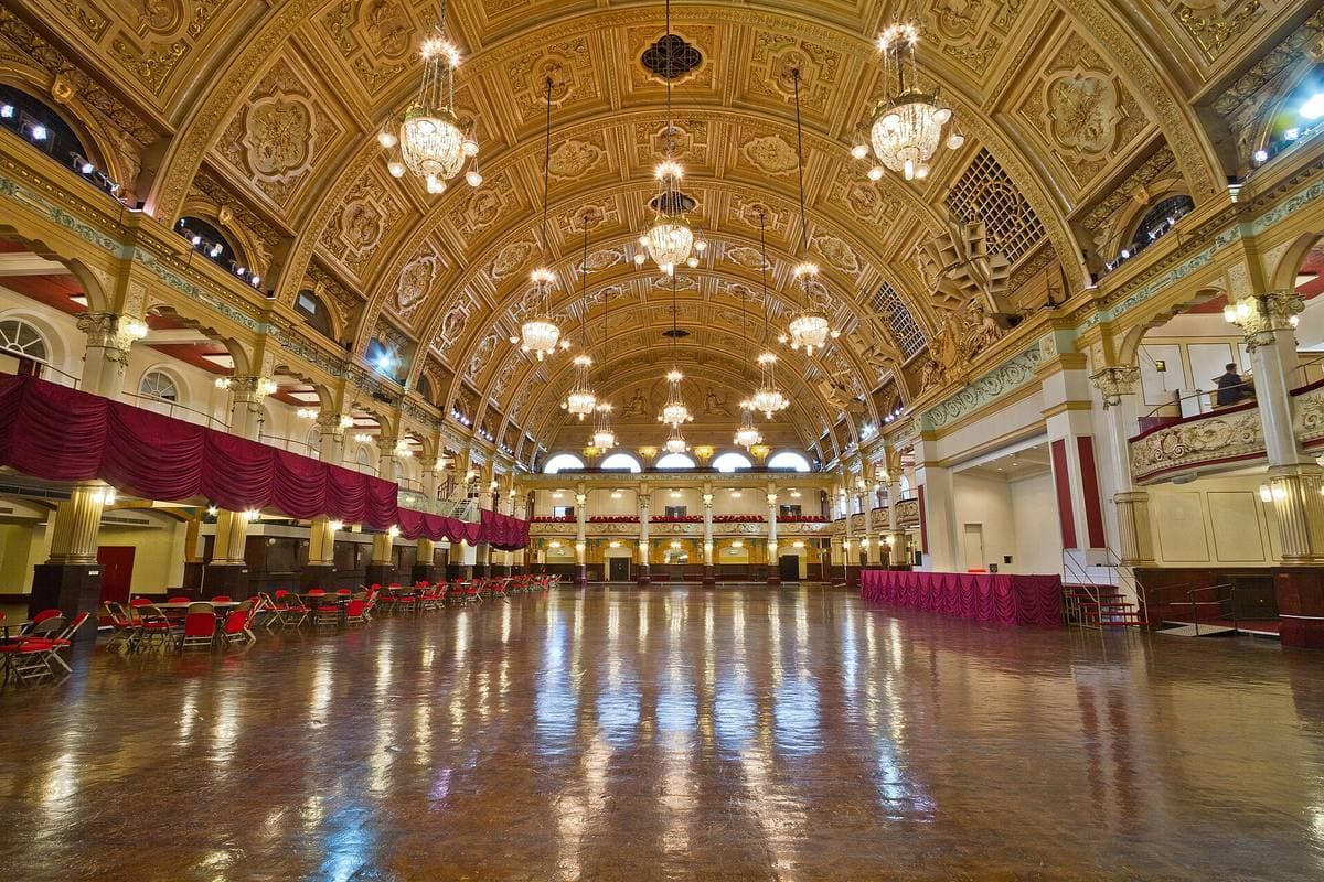 A vast gilded ballroom with a barrel-vaulted ceiling, chandeliers and a polished wooden floor