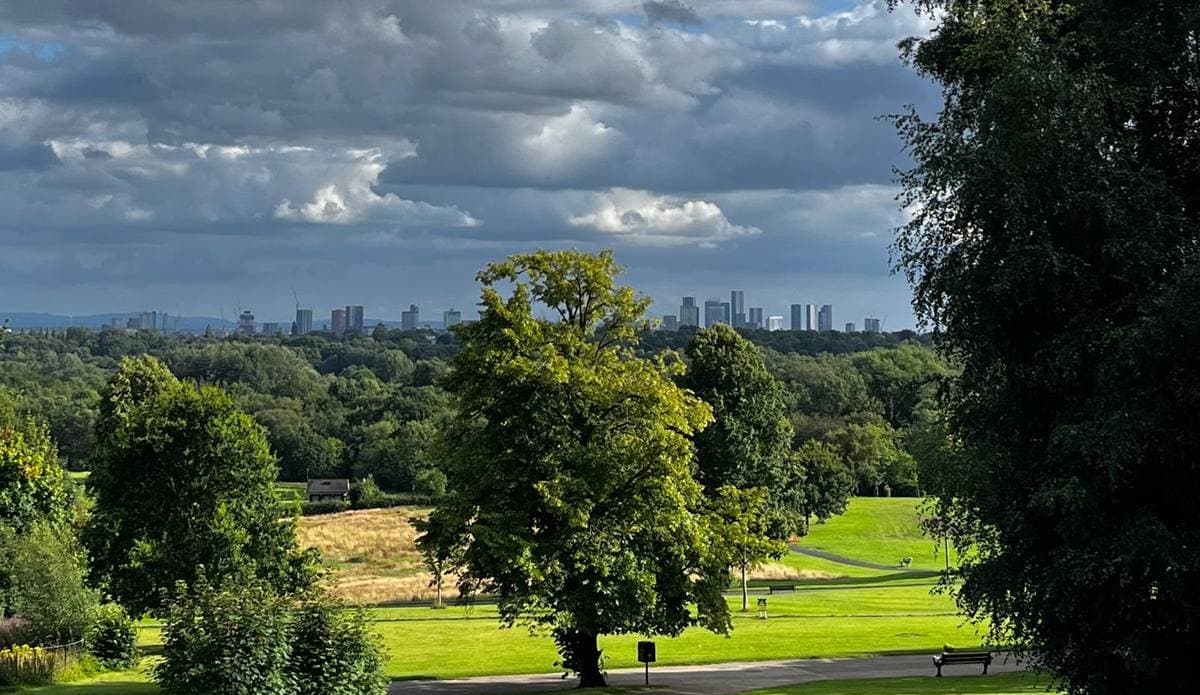 Green parkland and trees in the foreground, the Manchester skyline small on the horizon