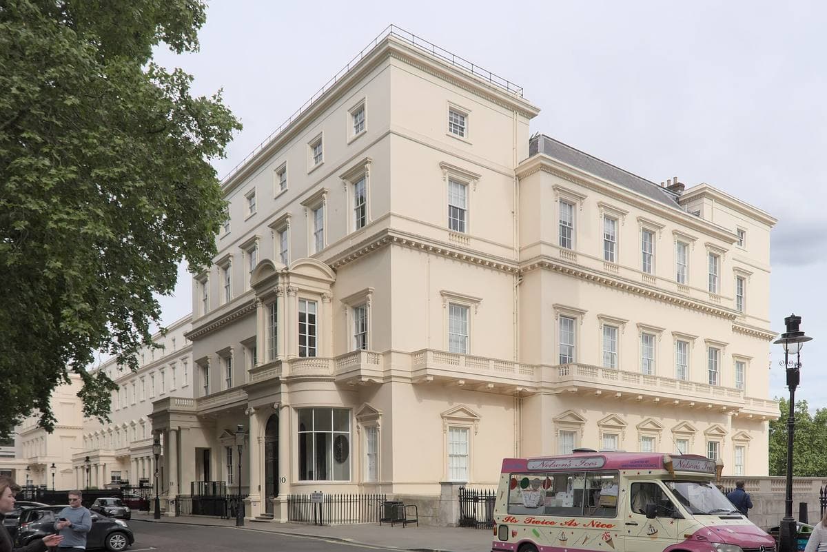 A tall cream stucco terrace building on a corner, a tree beside it and an ice-cream van at the kerb