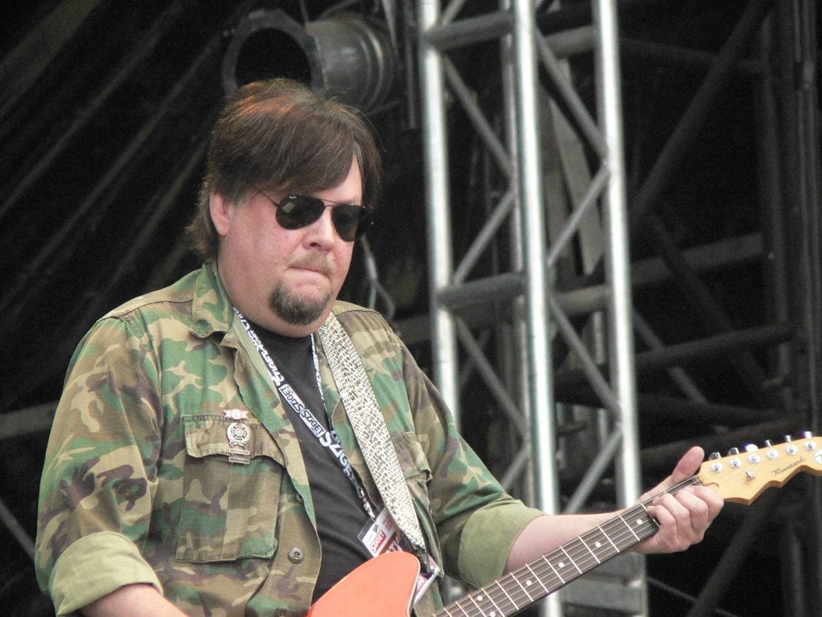A guitarist in black on a festival stage