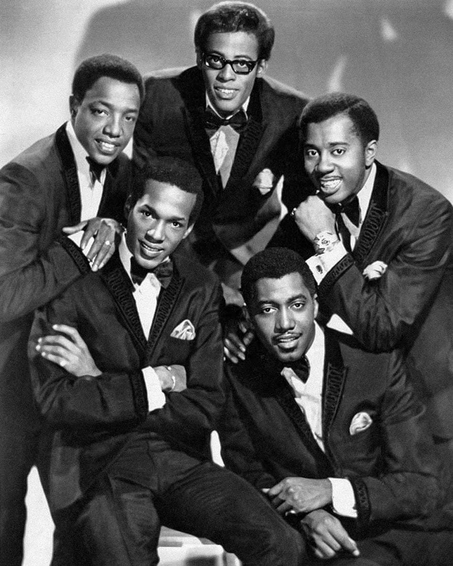 The five Temptations in dark tuxedos with bow ties, grouped and smiling