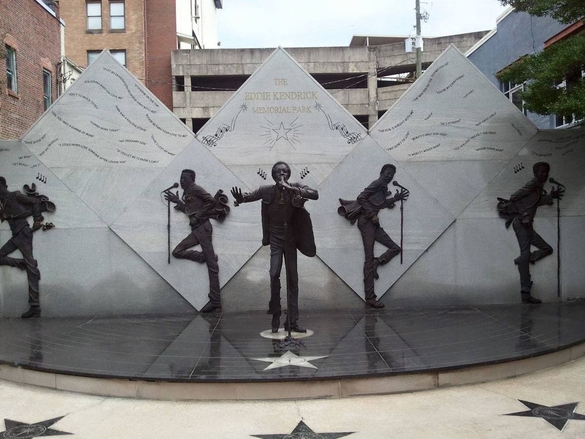A bronze statue of Eddie Kendricks with the other Temptations in relief on a granite wall