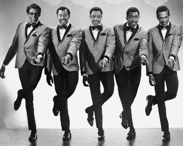 Five men in matching jackets lifting the same knee in perfect unison