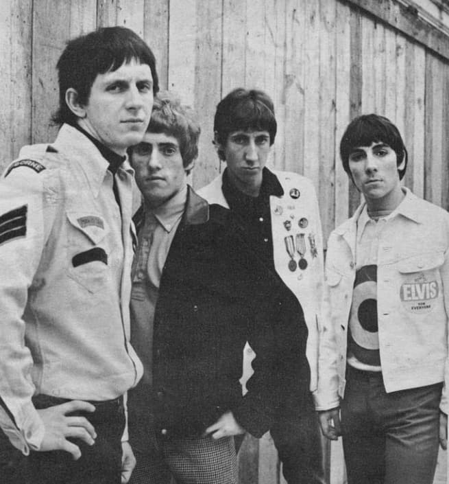 The four members of the Who against a wooden fence, Moon in a target T-shirt and Townshend in a jacket covered in medals and badges