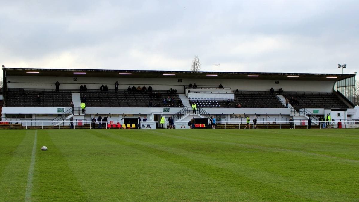 A rugby pitch with a stand and trees behind