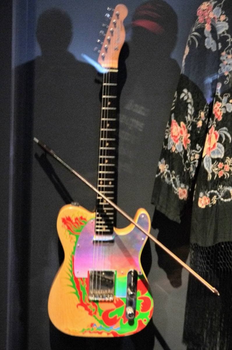 An electric guitar with a painted dragon on its body in a museum case