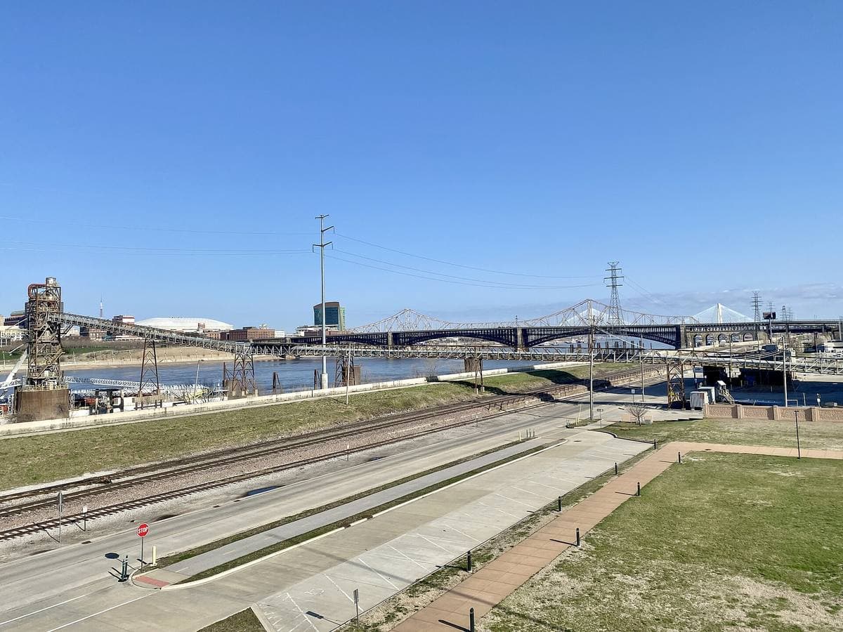 The arches of the Eads Bridge across a wide river from a riverside park