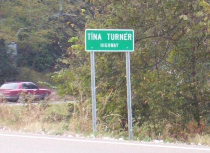 A small green road sign reading Tina Turner Highway at the roadside