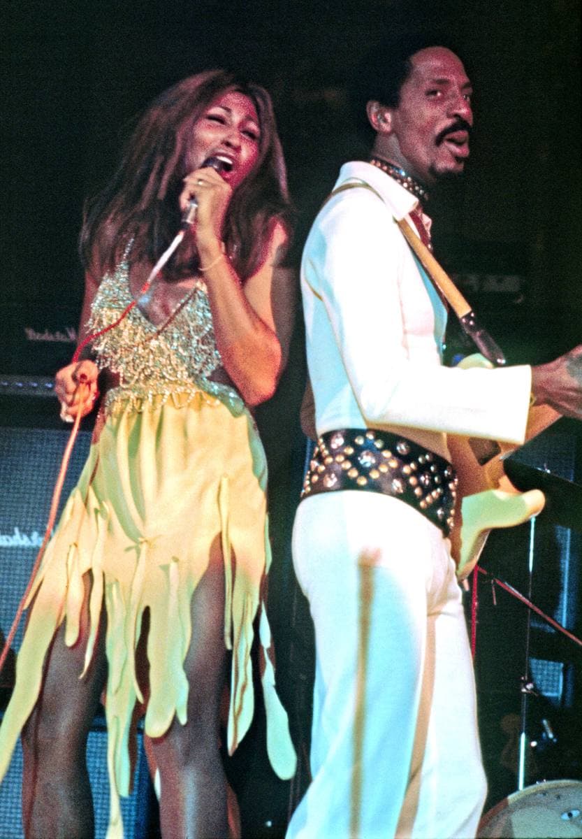 Tina Turner singing in a yellow fringed dress beside Ike Turner in white with a guitar