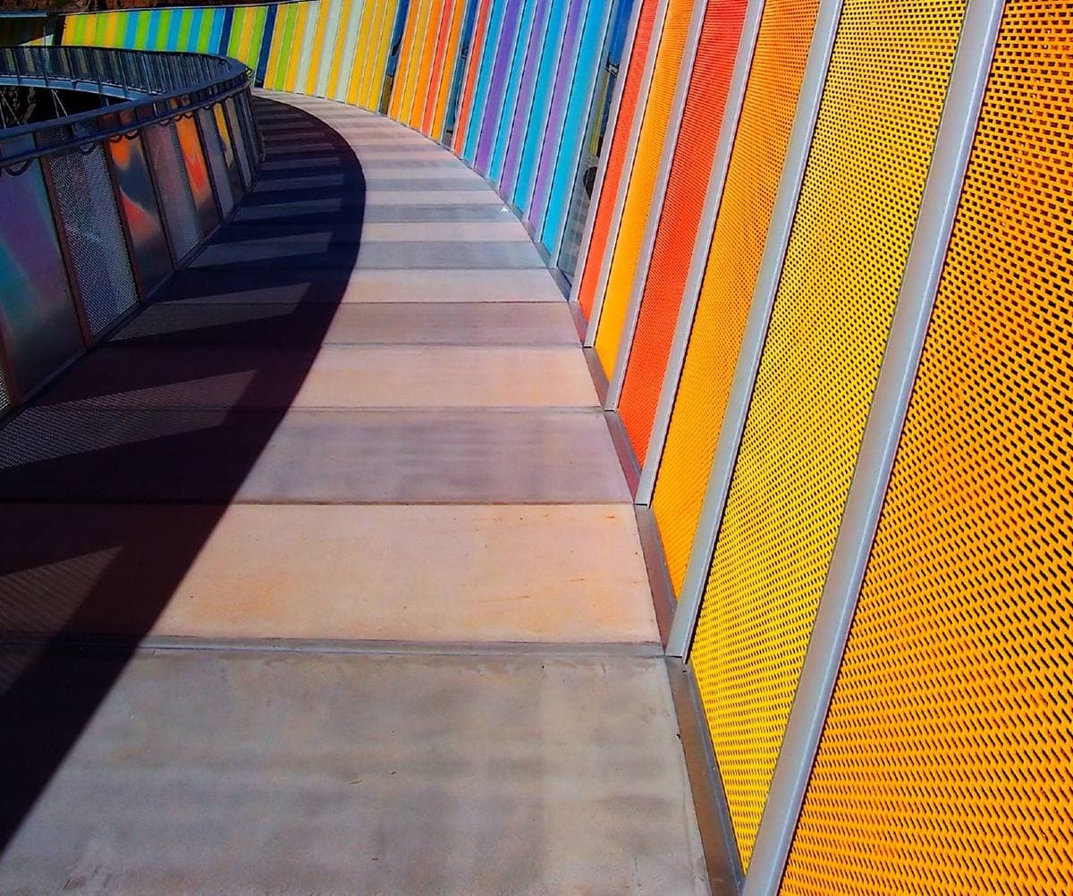 A curved elevated walkway lined with panels in every colour