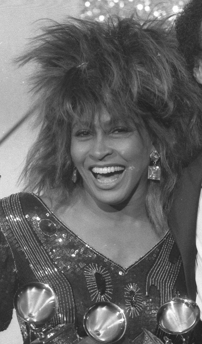 Tina Turner laughing under a huge spiky blonde-brown wig, in a sequinned top