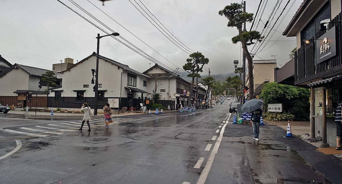 A wide wet street lined with low traditional buildings and pines under cloud