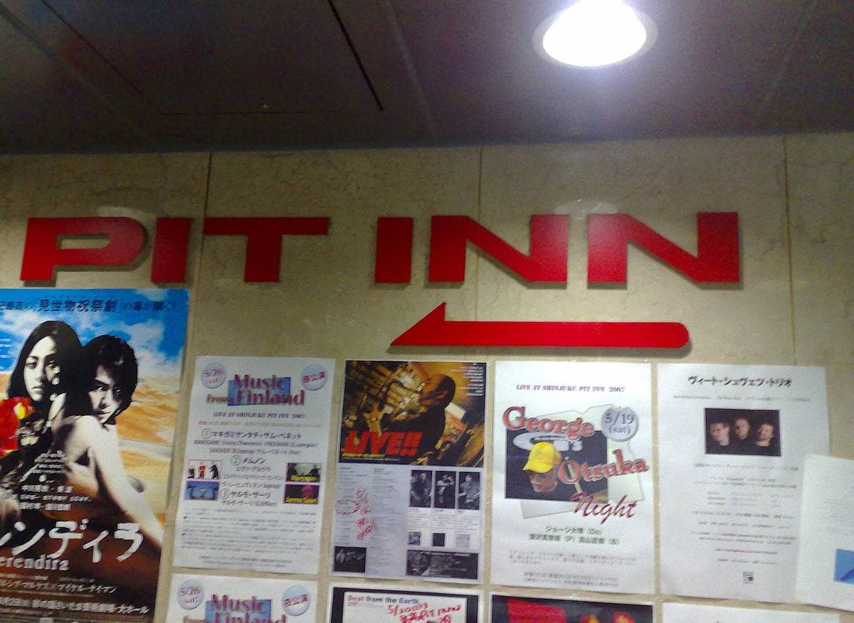 A white wall with the red letters PIT INN and an arrow above concert flyers