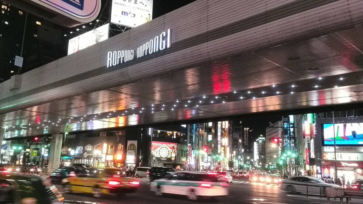 Taxis streaking under an elevated expressway lit up at night in Roppongi