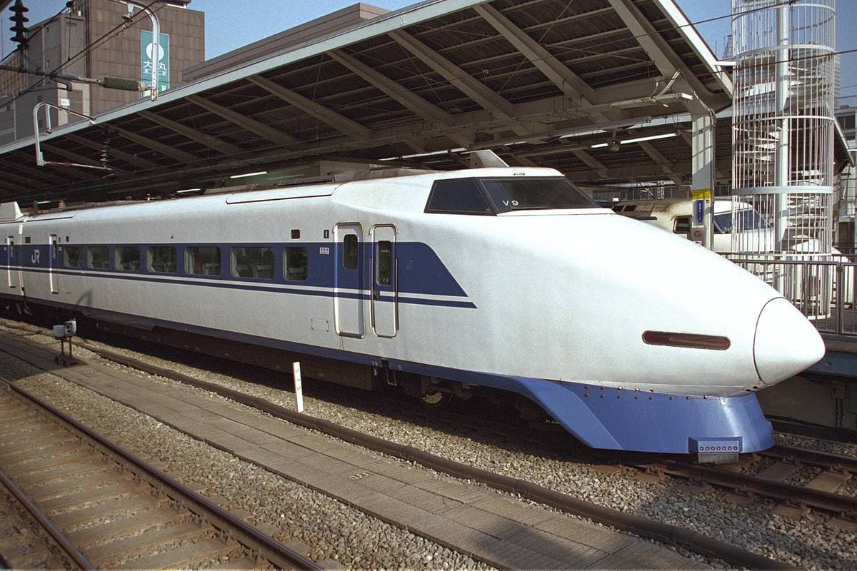 A white Shinkansen with a long pointed nose and blue stripe at a platform