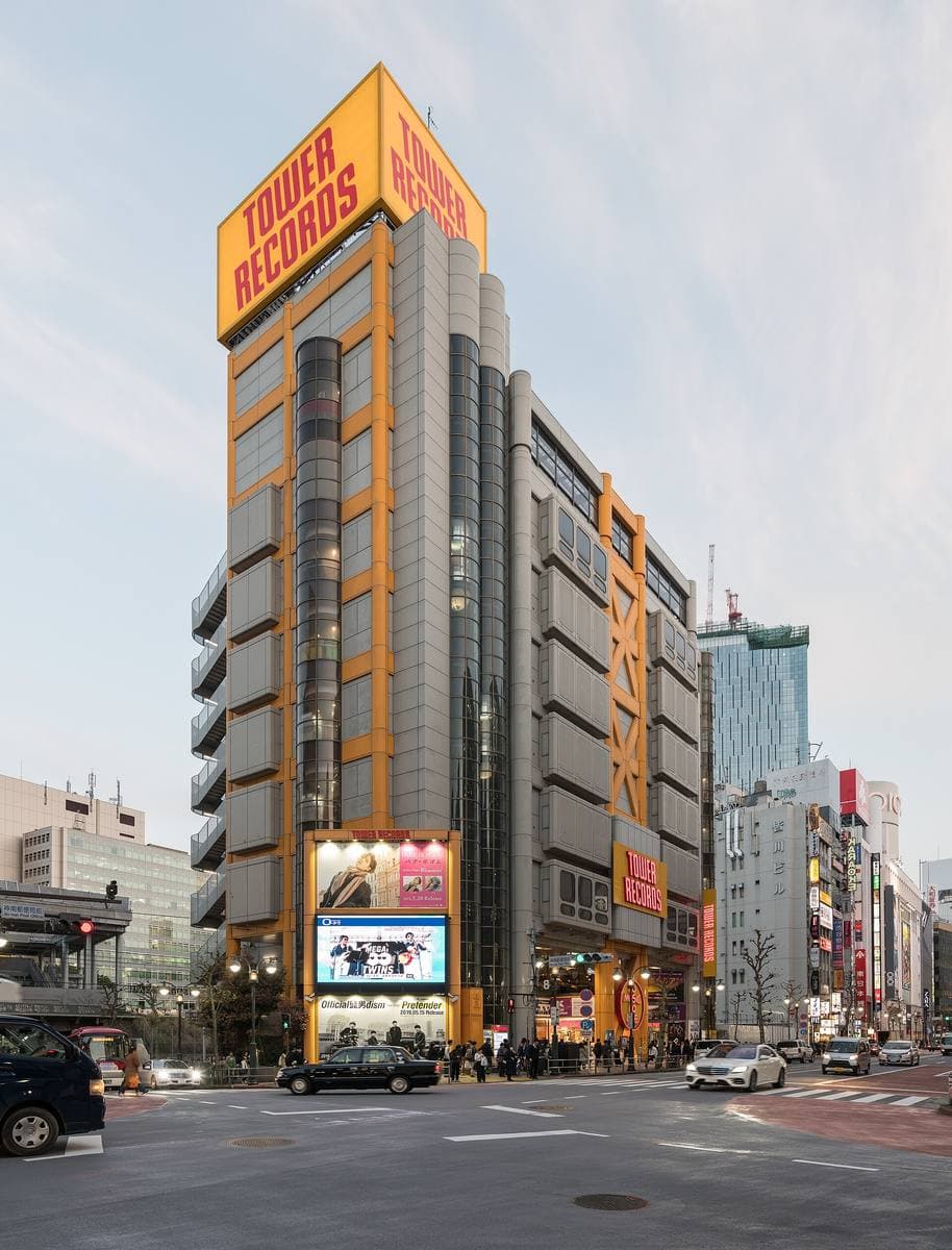 A tall grey building with yellow and red Tower Records signs on a Shibuya corner
