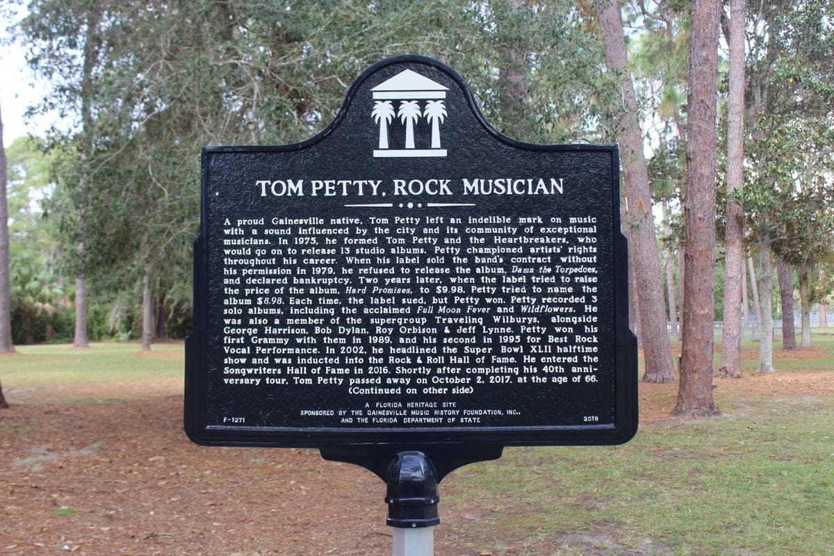 A black Florida historical marker titled Tom Petty, Rock Musician, standing under pine trees