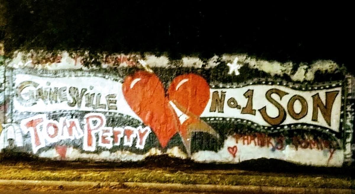 A painted wall panel at night with a red heart and the words Gainesville’s No. 1 Son and Tom Petty