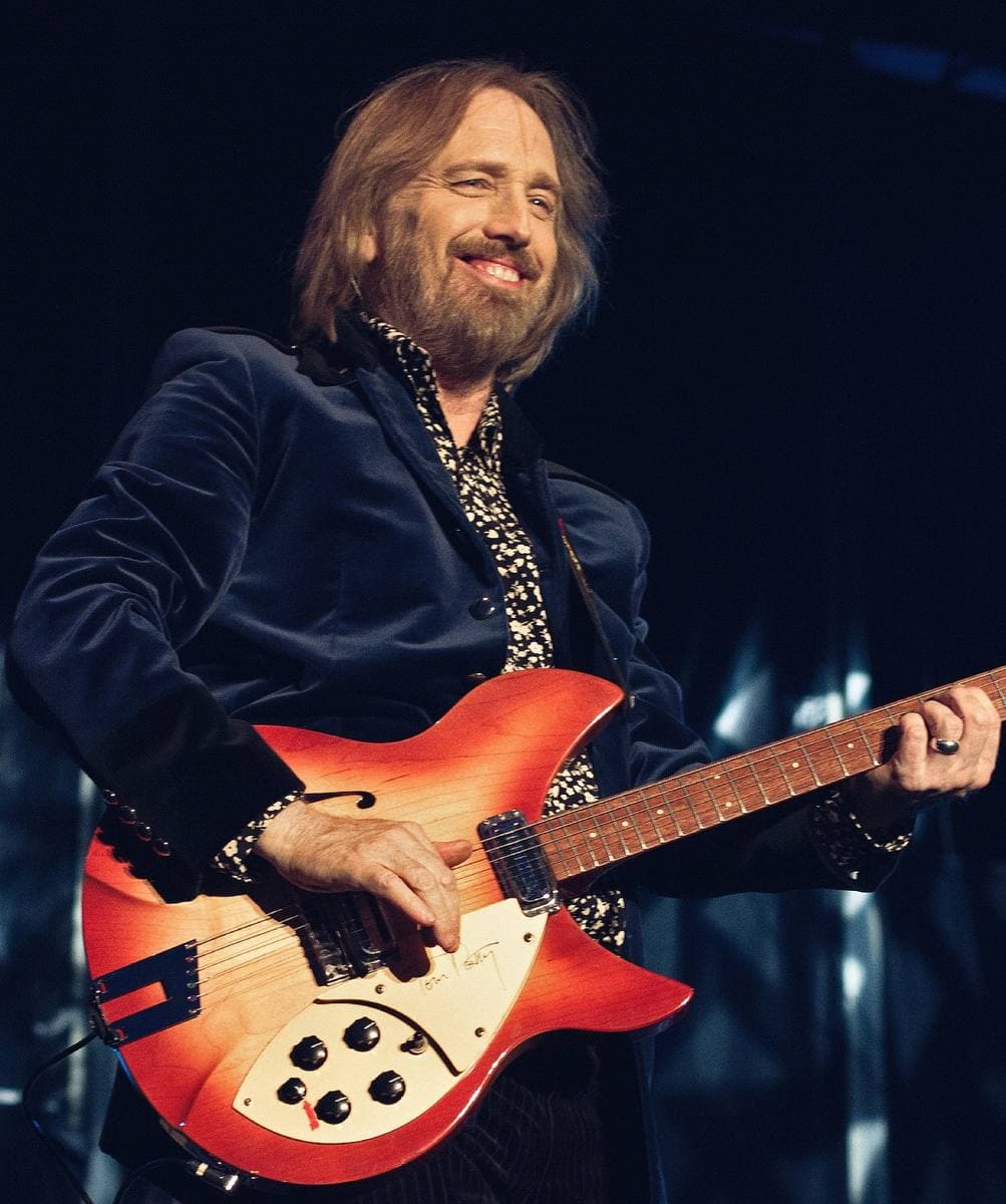 Tom Petty singing at a microphone in a dark velvet jacket, playing a red Rickenbacker guitar