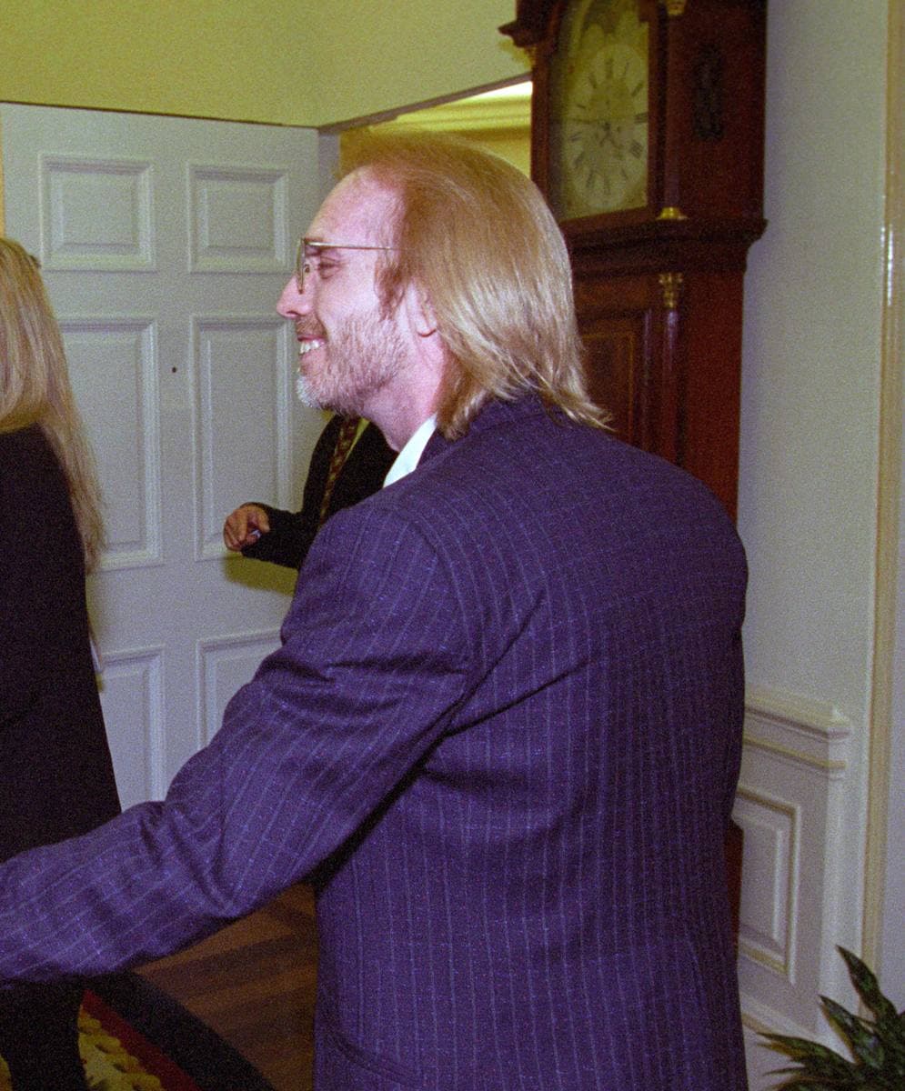 Tom Petty with long fair hair, glasses and a purple pinstripe suit, smiling