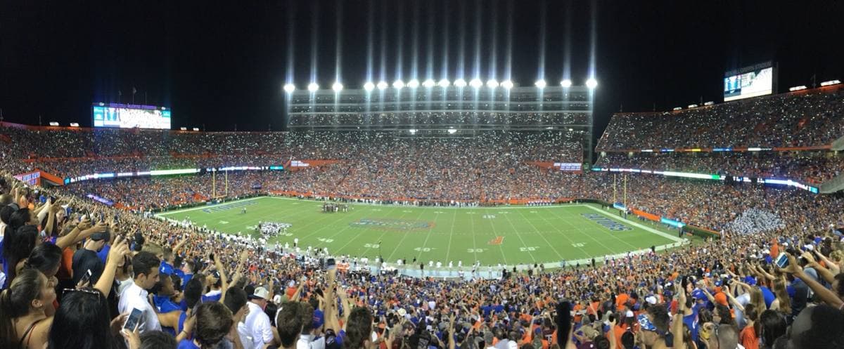 A packed football stadium at night under floodlights, the crowd on its feet