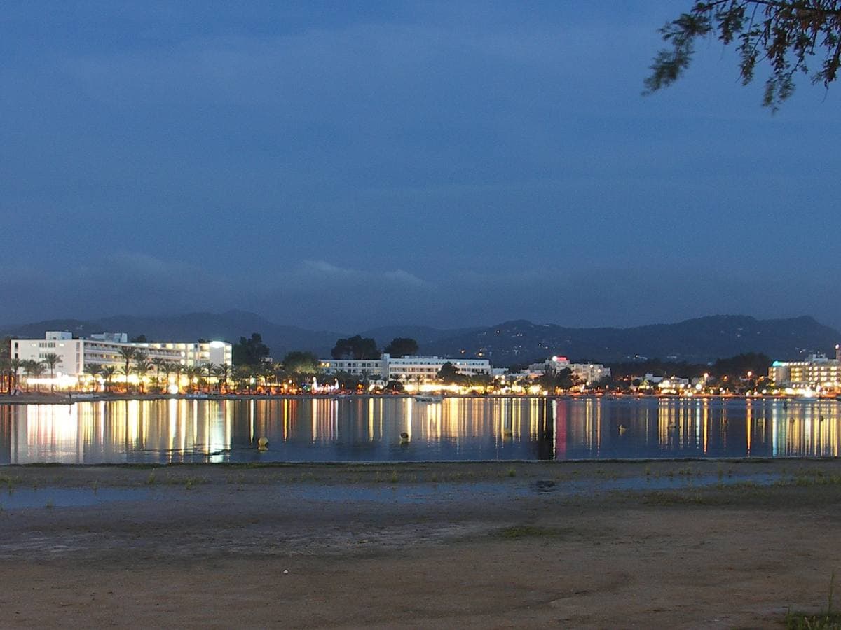 The lights of a seaside town reflected in a calm bay at dusk