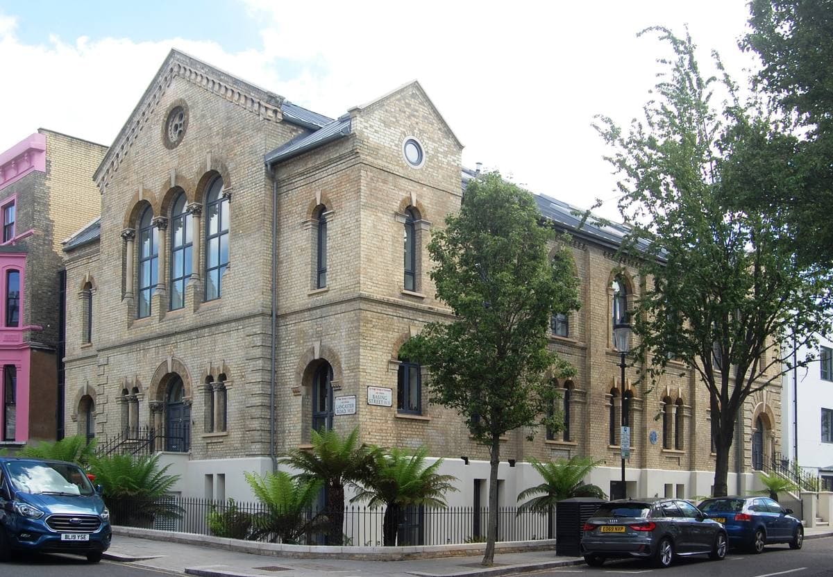 A pale stone Victorian chapel with round-arched windows on a quiet Notting Hill street, now flats