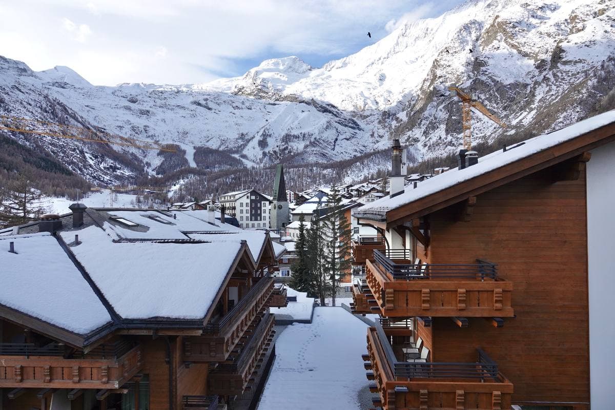 Snow-covered chalet roofs and a church spire in a valley under high snowy peaks
