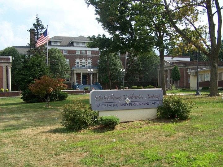 A brick school building behind a lawn and a sign for the Whitney E. Houston Academy
