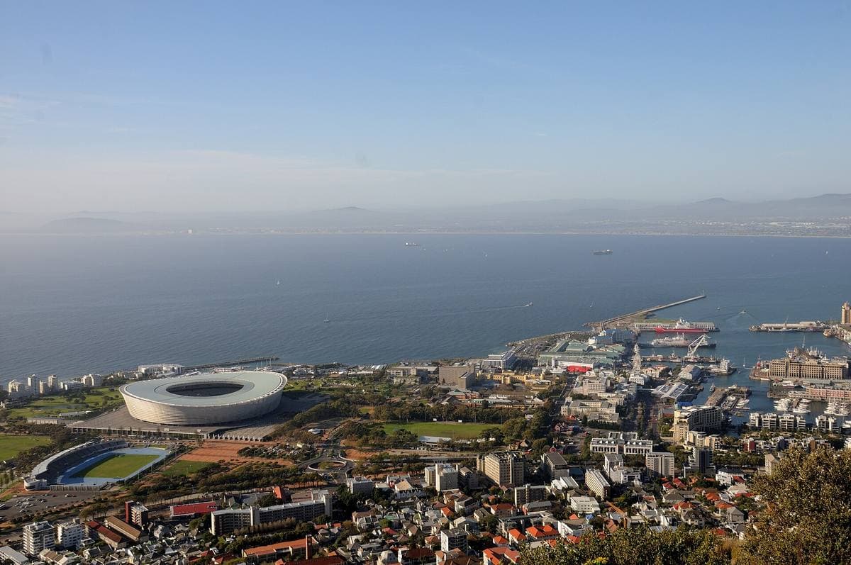 A round white stadium near the harbour and the sea, seen from a hill above Cape Town
