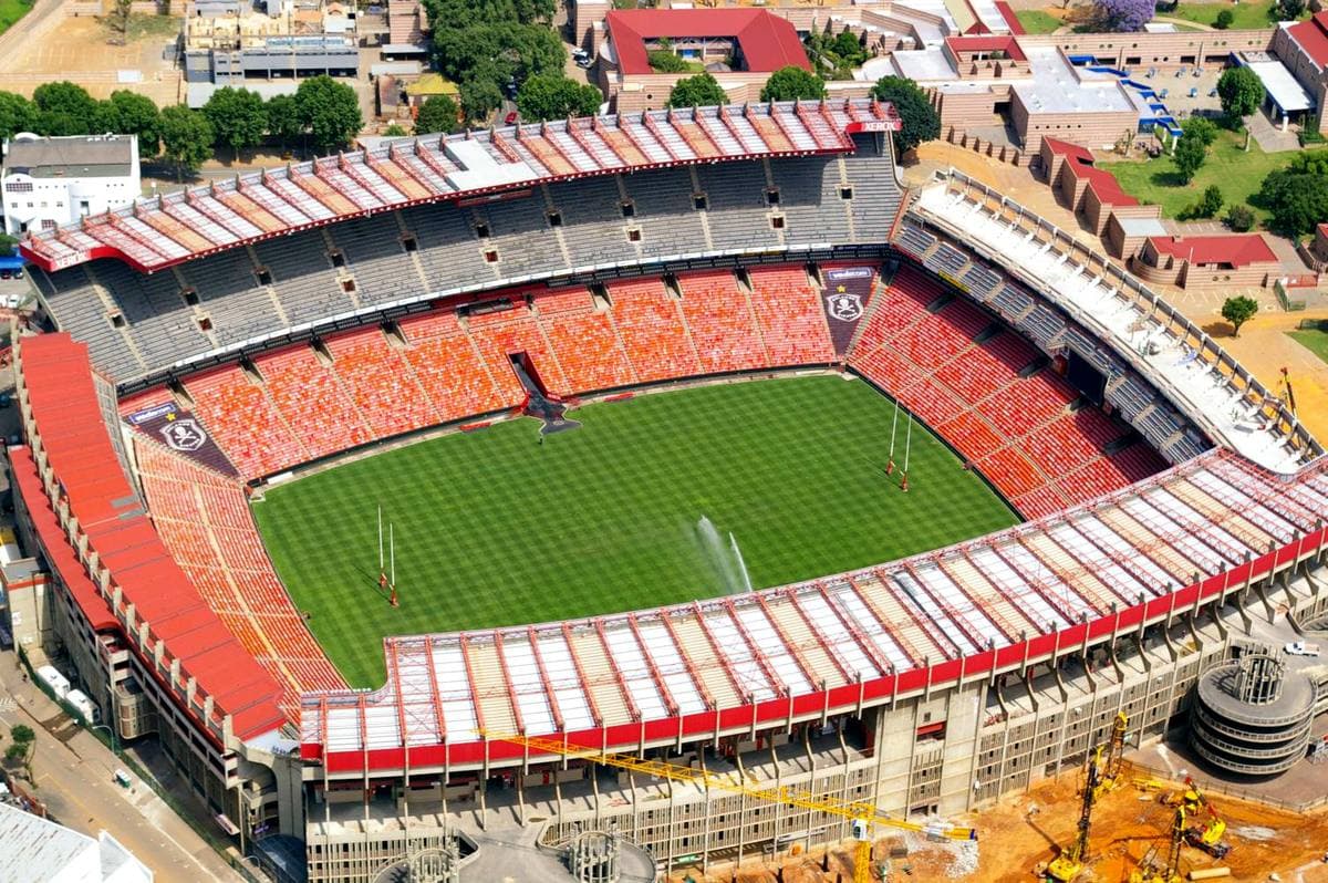 A bowl stadium with red seats and a green pitch seen from above