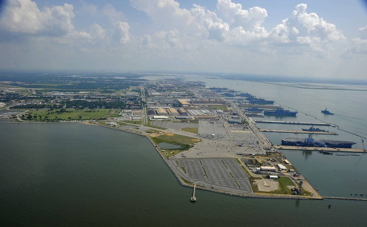 An aerial view of a naval base with piers and grey ships on the water