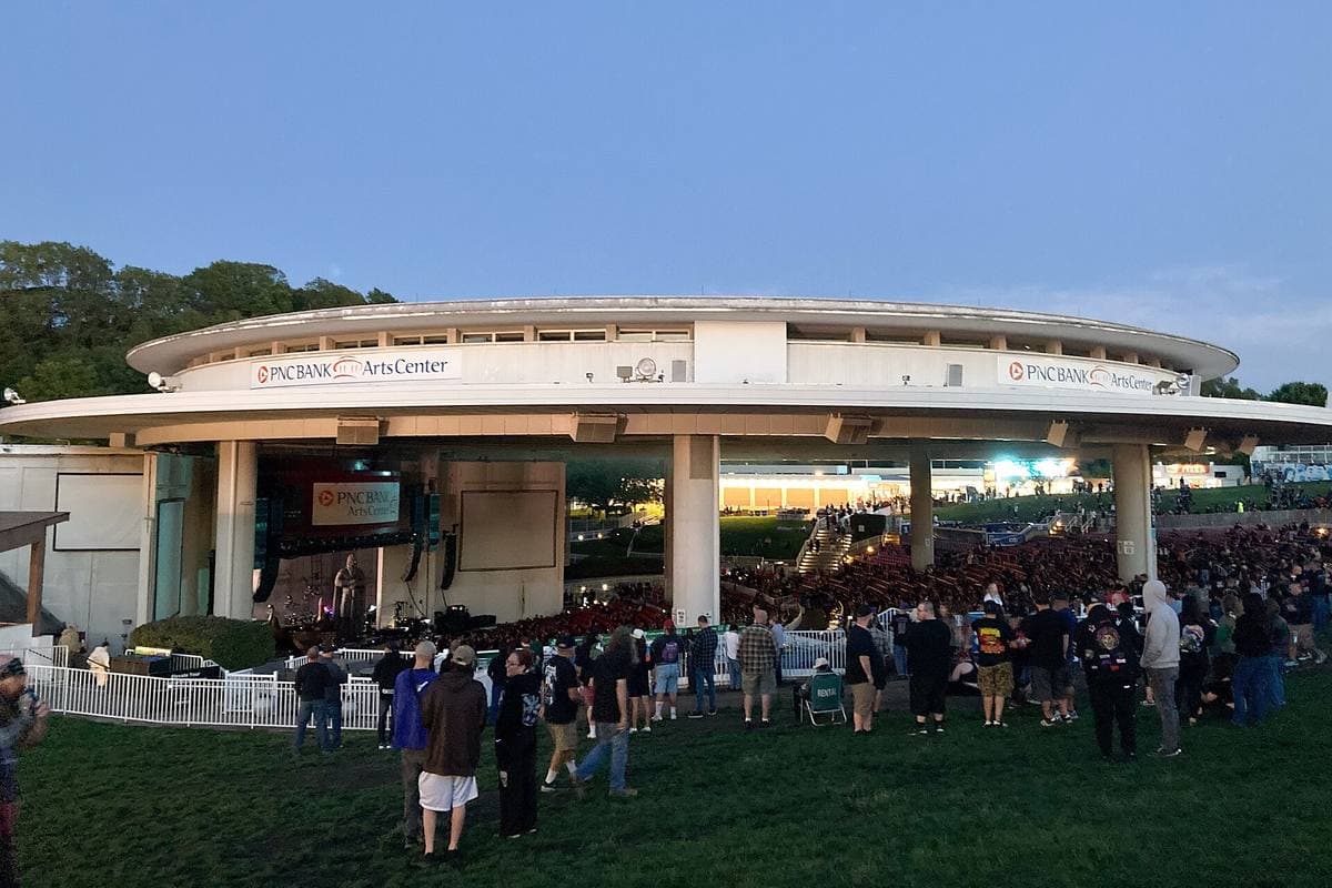 A round open-sided amphitheatre roof over a crowd on the lawn at dusk