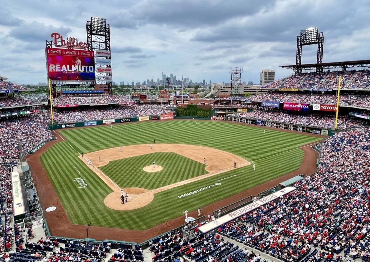 A baseball park seen from the upper deck, green field and red seats under a blue sky