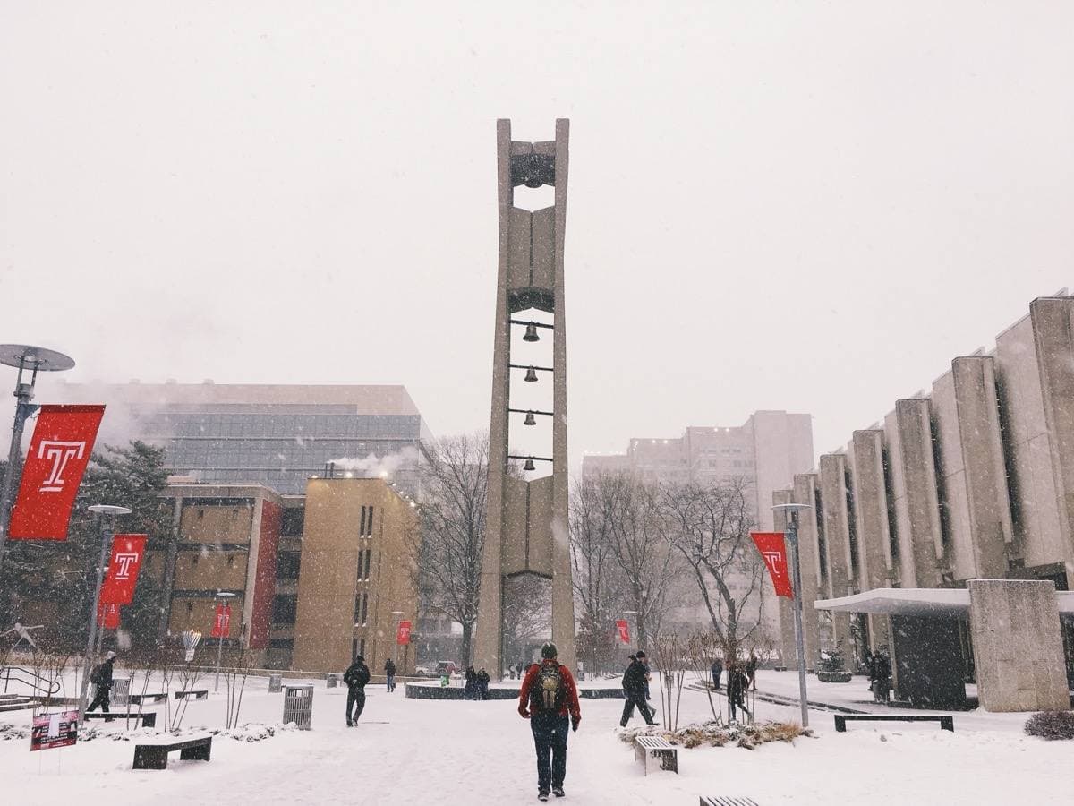 A tall modern bell tower on a campus lawn with snow on the ground
