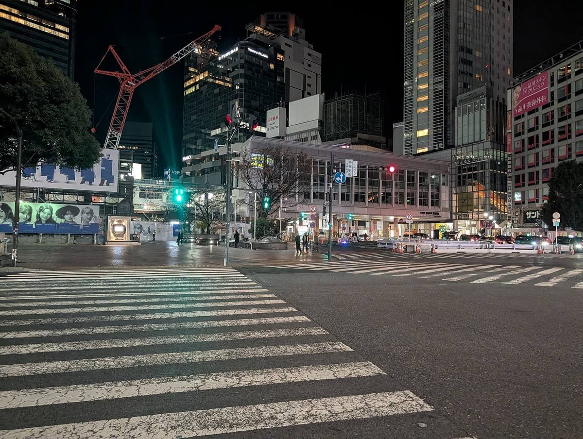 Shibuya Scramble Crossing at night with no one on its zebra stripes, lit towers behind