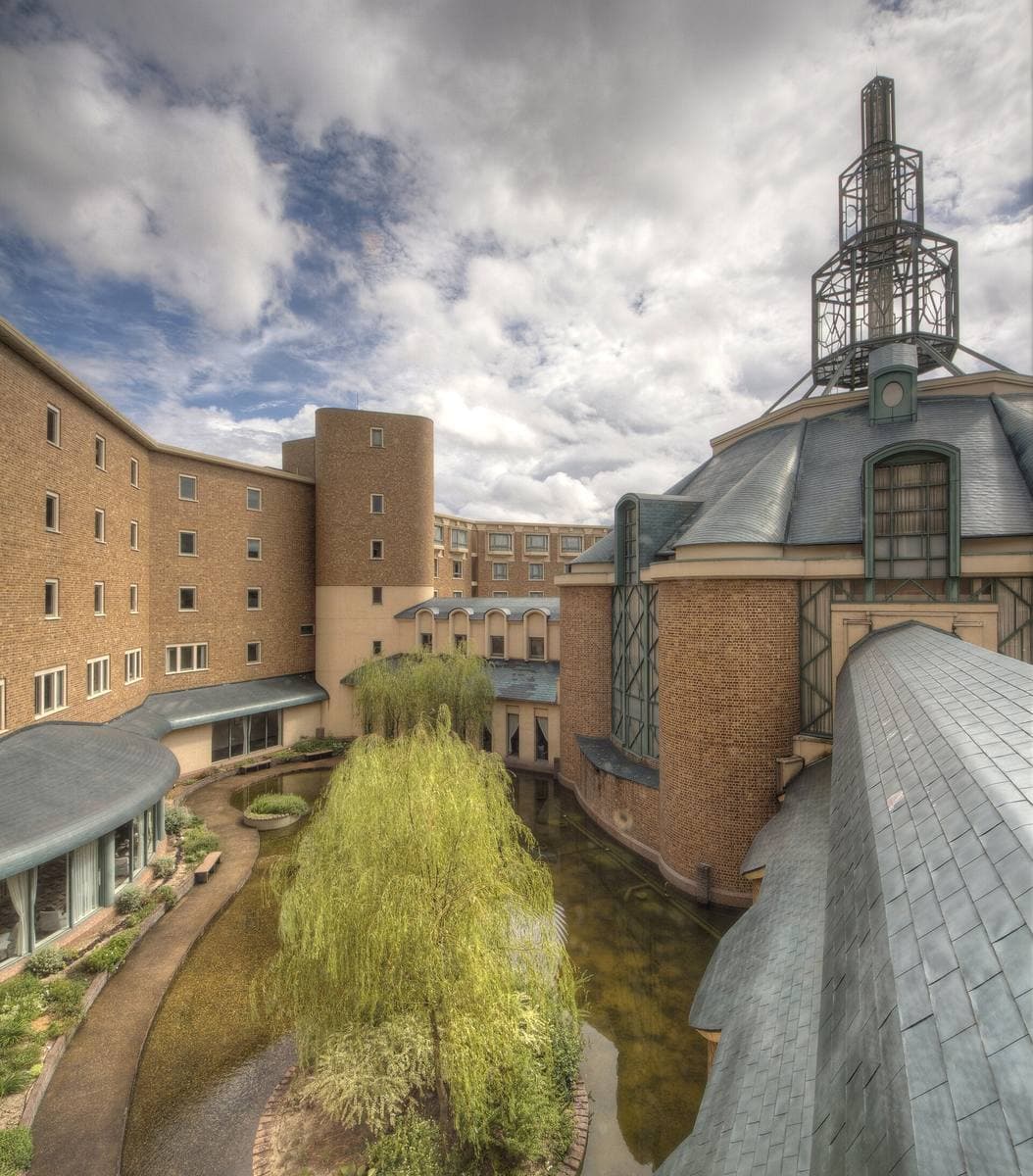A brick-coloured hotel wing round a courtyard garden with a willow, a spired tower above